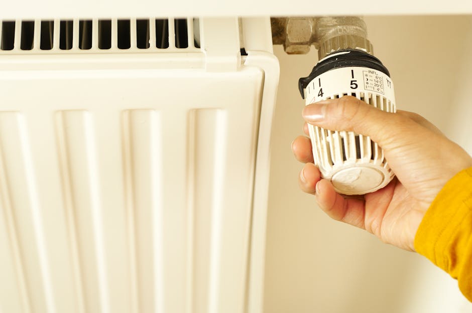 Žmogus reguliuoja termostatą šviesiame kambaryje, matoma šildymo automatika